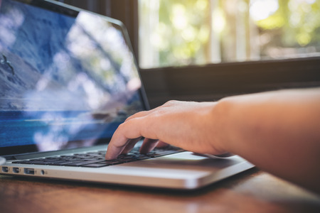 Closeup image of a business woman's hands working and typing on laptop keyboard on wooden table