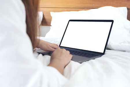 Mockup image of a woman lying on a bed , using and typing on laptop with blank white desktop screen keyboardの写真素材