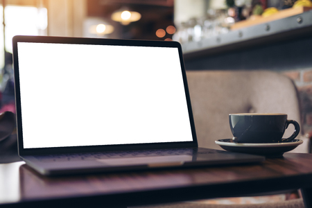 Mockup image of laptop with blank white desktop screen and coffee cup on wooden table in modern cafeの写真素材