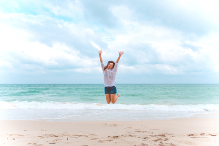 A woman jumping on the beach in front of the sea with feeling happy and freedomの写真素材