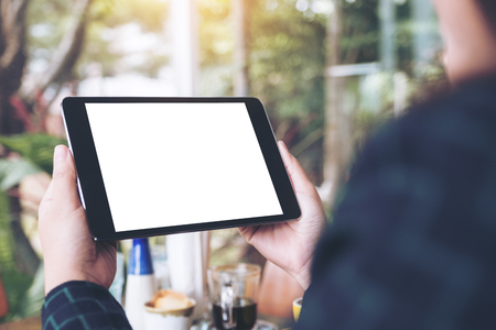 Mockup image of business woman's hands holding black tablet pc with blank desktop white screen in cafe and green nature backgroundの写真素材