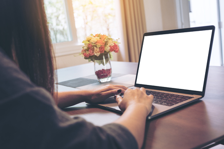 Mockup image of woman's hands using and typing on laptop with blank white desktop screen on wooden table in the houseの写真素材