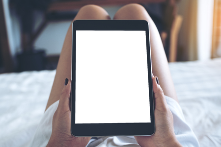 Mockup image of woman's hands holding black tablet pc with blank desktop white screen while lying in a white bed with feeling relaxedの写真素材