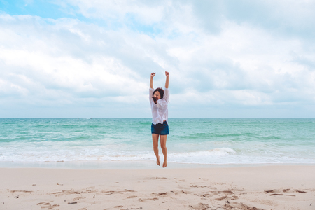 A woman jumping on the beach in front of the sea with feeling happy and freedomの写真素材