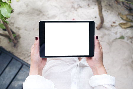 Mockup image of a woman's hand holding black tablet pc with blank white desktop screen with sand and beach backgroundの写真素材
