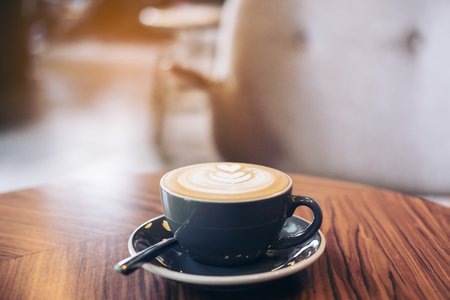 Closeup image of a blue cup of hot latte coffee with latte art on vintage wooden table in cafeの写真素材