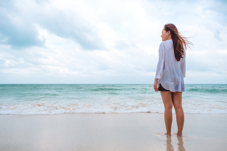 An Asian woman standing and looking at view on the beach with the sea and blue sky backgroundの写真素材