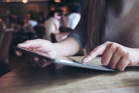 Closeup image of a woman's hands pointing , touching and using tablet pc  on wooden table in cafeの写真素材