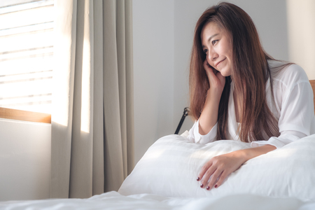 Portrait image of a beautiful Asian woman sitting on the bed after woke up with feeling happy and relaxedの写真素材