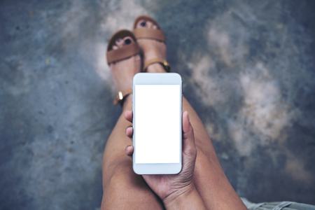 Top view mockup image of a woman sitting and holding white mobile phone with blank desktop screen の写真素材