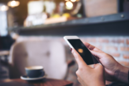 Blur image of a woman holding and using smart phone in modern cafeの写真素材