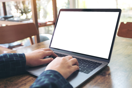 Mockup image of hands using and typing on laptop with blank white desktop screen on wooden table in cafeの写真素材