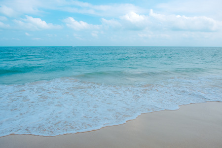 Waves on tropical white beach with blue sky background