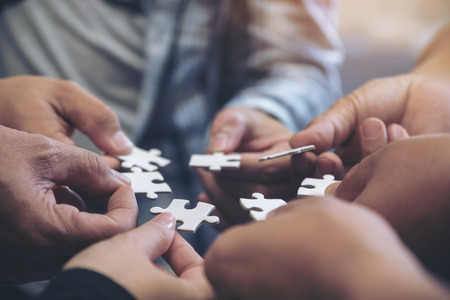Closeup image of many people hands holding a jigsaw puzzle in circle together