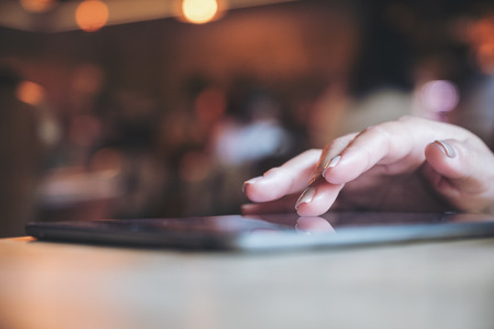 Closeup image of a woman's hand pointing , touching and using tablet pc with blur background in cafeの写真素材