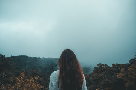 A woman standing alone looking at white foggy and mountains backgroundの写真素材