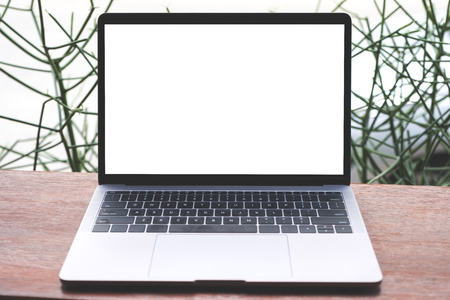 Mockup image of laptop with blank white screen on vintage wooden table with green plant in backgroundの写真素材