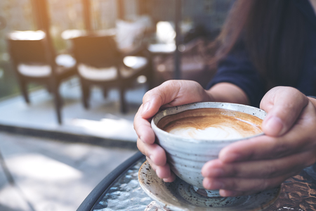 Closeup image of hands holding a cup of hot coffee on glass table in cafeの写真素材