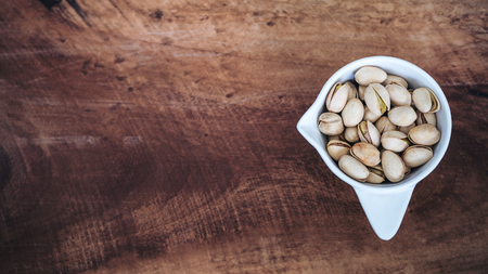 Top view image of pistachios in a white cup on wooden backgroundの写真素材
