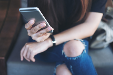 Closeup image of a woman's hand holding and using at smart phone sitting cross leg in modern cafeの写真素材