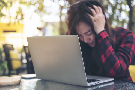 Closeup image of an Asian business woman with feeling stressed and tired , close her eyes while using laptop on glass table sitting at outdoor with green nature backgroundの写真素材