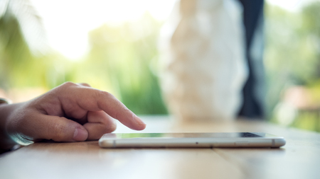 A woman using and touching smart phone on the table in modern cafe with blur green nature background