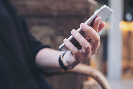 Closeup image of a  woman's hands holding , using and looking at smart phone in modern cafeの写真素材