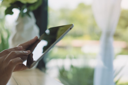 Closeup image of a woman's hands holding , typing and using tablet pc  on wooden table in cafeの写真素材