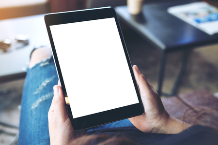 Mockup top view image of a woman sitting cross legged and holding black tablet pc with blank white screen on thigh in cafeの写真素材