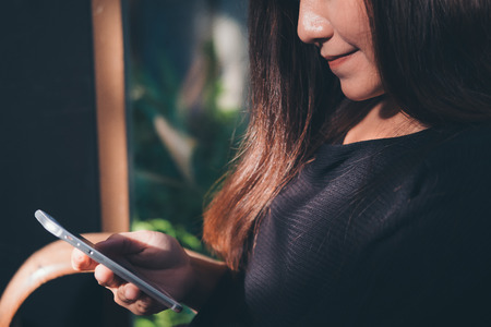 Closeup image of a beautiful Asian woman with smiley face using and looking at smart phone in modern cafeの写真素材