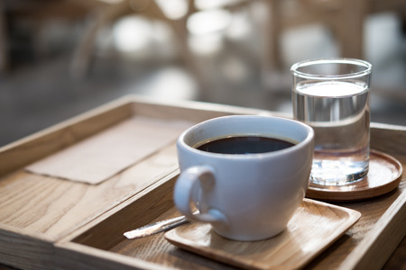 Closeup image of a cup of hot coffee and a glass of water in vintage wooden tray on the table in cafeの写真素材