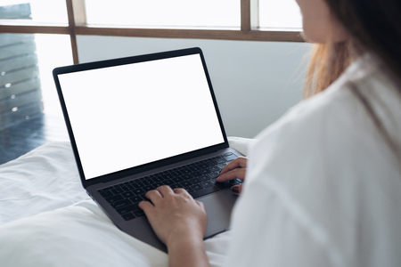 Mockup image of an Asian woman sitting on a bed , using and typing on laptop with blank white desktop screen keyboardの写真素材