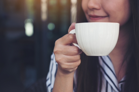 Closeup image of Asian woman smelling and drinking hot coffee with feeling good in cafeの写真素材