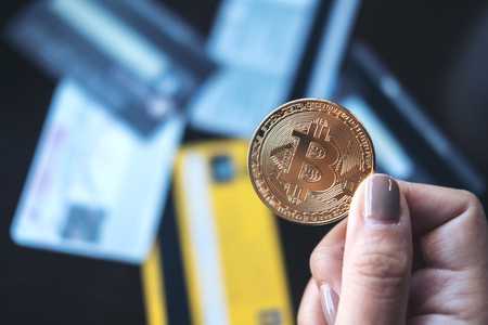 Closeup image of a woman holding a golden color bitcoin with many credit cards on table in officeの写真素材