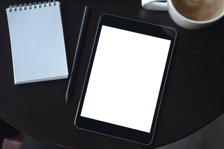 Top view mockup image of a black tablet pc with blank white desktop screen with notebook and coffee cup on the tableの写真素材