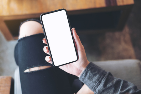 Top view mockup image of a woman holding white mobile phone with blank black desktop screen on thigh in cafeの写真素材