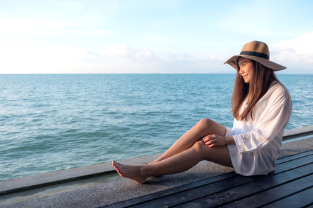 Portrait image of a happy beautiful asian woman on white dress sitting on wooden balcony by the sea with clear blue sky backgroundの写真素材