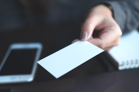 Business woman holding and giving  business card to someone with mobile phone and notebook on table in officeの写真素材