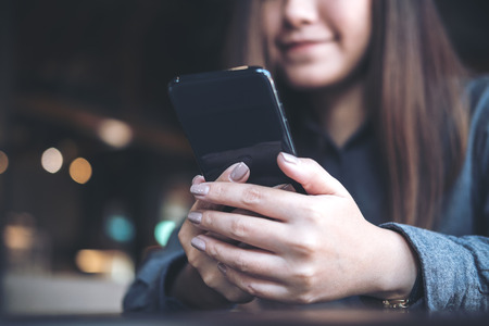 Closeup image of a beautiful Asian woman holding , using and looking at smart phone in modern cafeの写真素材