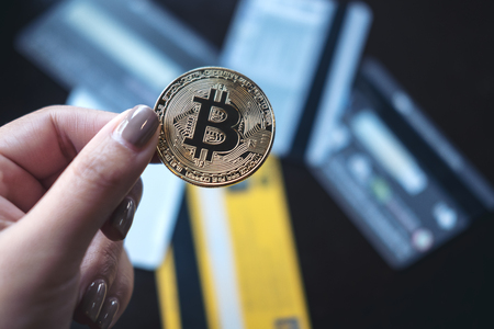 Closeup image of a woman holding a golden color bitcoin with many credit cards on table in officeの写真素材
