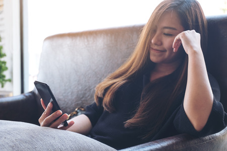 Closeup image of a beautiful Asian woman holding , using and looking at smart phone with feeling happyの写真素材