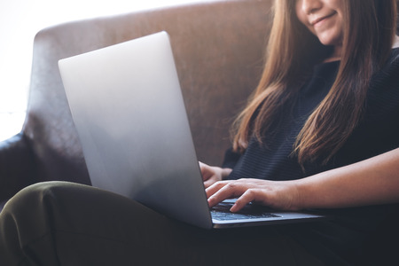 Closeup image of an Asian woman working and typing on laptop keyboard while sitting on sofaの写真素材