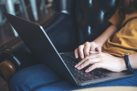 Closeup image of woman's hands working and typing on laptop keyboard while sitting on sofa