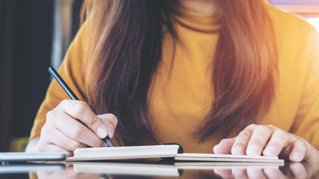 Close up image of a woman writing on notebook with coffee mug on wooden table in cafeの写真素材