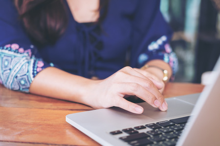 Closeup image of an Asian business woman's hands working and typing on laptop keyboard on wooden tableの写真素材