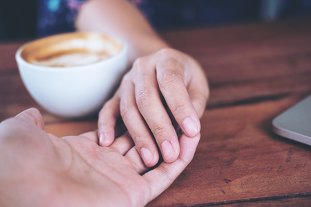 A man and a woman holding each other hands with feeling love on wooden table backgroundの写真素材