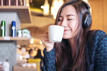 A beautiful Asian woman close her eyes and listening to music with headphone while drinking coffee with feeling happy and relax in modern cafeの写真素材