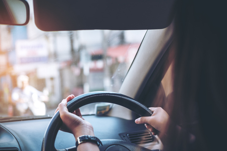 Woman holding on black steering wheel while driving a car with traffic background