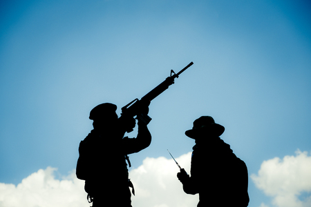 Silhouette image of two armed soldiers with blue sky backgroundの写真素材