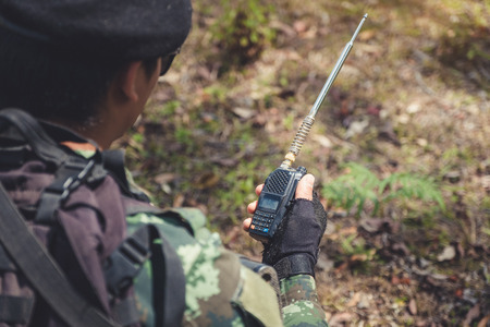 Closeup image of an armed soldier holding and using radio communication in the battle fieldの写真素材